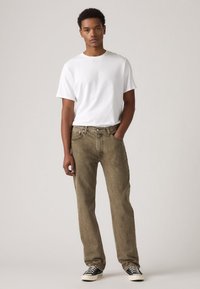 T-shirt blanc léger à manches courtes, associé à un jean droit vert olive délavé et des baskets noir et blanc.