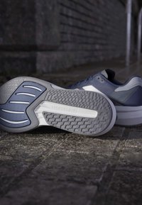 Modrá športová obuv s šedou, textúrovanou podrážkou, ktorá má gumový a vzorovaný povrch, vyrazené logo "LIGHTSTRIKE" a aerodynamický dizajn.