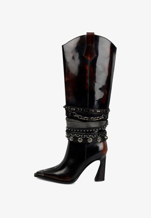 Stivale nero in pelle alto fino al ginocchio con punta appuntita, caratterizzato da cinghie e catene in metallo borchiato attorno alla caviglia. Design con tacco a spillo.