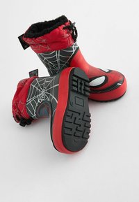 Bottes de neige pour enfants rouges et noires avec un design de toile d'araignée et une doublure en fausse fourrure. Semelles en caoutchouc crantées pour une meilleure adhérence. Partie supérieure avec cordon de serrage.