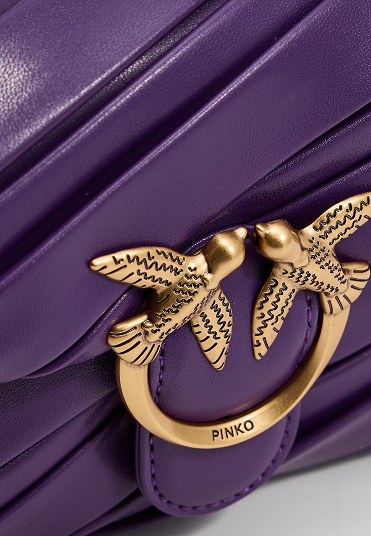 Borsa a tracolla in pelle viola con design trapuntato, dettagli in metallo dorato a forma di uccello e un anello circolare con branding.