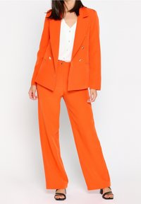 Orange blazer and matching wide-leg pants made of smooth fabric. Blazer features double-breasted design with gold buttons; paired with a white shirt.