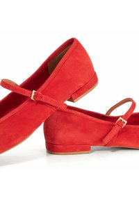 Paar rode suede Mary Jane-schoenen met lage blokhakken en verstelbare goudkleurige gespbandjes op een witte achtergrond.