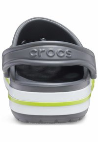Szare plastikowe Crocs z grubą białą podeszwą i żółtym paskiem akcentującym. Posiadają okrągły wzór wentylacyjny oraz tylny pasek zapewniający stabilne dopasowanie.