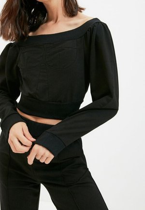 Schwarzes, schulterfreies Crop-Top mit langen gepufften Ärmeln, gerippten Bündchen und einer Vorderseitentasche, aus glattem, dehnbarem Stoff gefertigt.