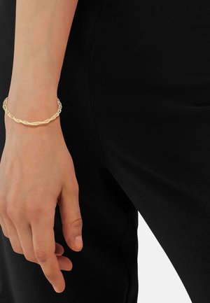 Bracciale color oro con design a catena intrecciata e maglie texture, indossato su una mano contro uno sfondo nero.