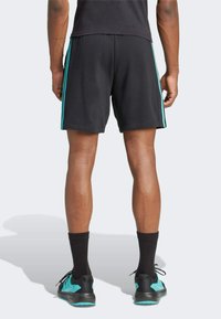 Pantalones cortos deportivos negros con rayas turquesas en los laterales, hechos de una tela suave, con un corte holgado y longitud por encima de la rodilla.