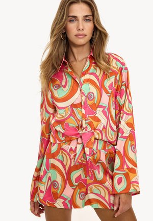 Kleurrijke oversized blouse met een draaiend abstract patroon in roze, oranje en muntgroen, met een getailleerde taille en lange mouwen.