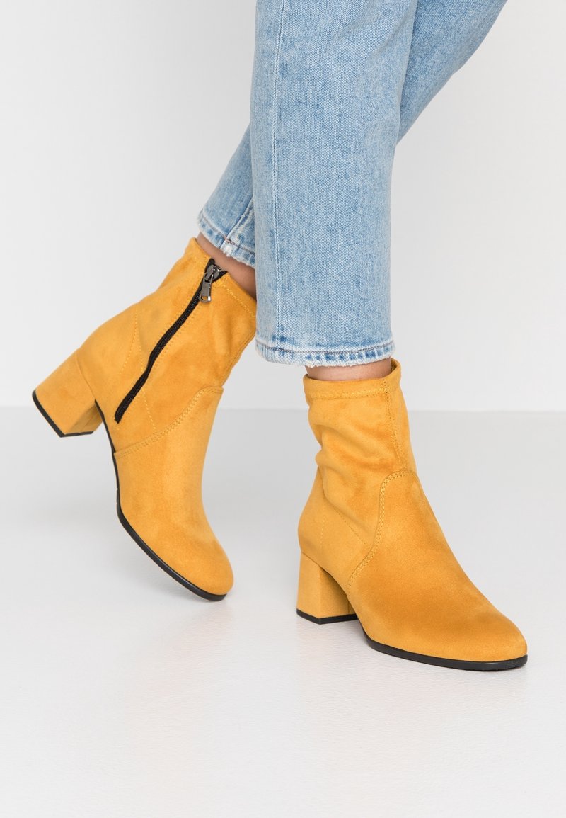 Bottines en suède jaune avec un talon carré, détail de fermeture éclair sur le côté et texture douce, associées à un jean crop bleu clair.