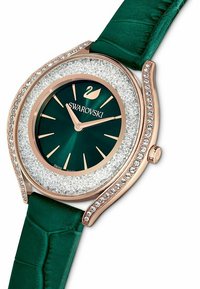 Swarovski-Uhr mit einem grünen Lederarmband, einem roségoldenen Gehäuse und Kristallakzenten. Das Ziffernblatt hat ein dunkelgrünes Ziffernblatt und goldene Stundenmarkierungen.