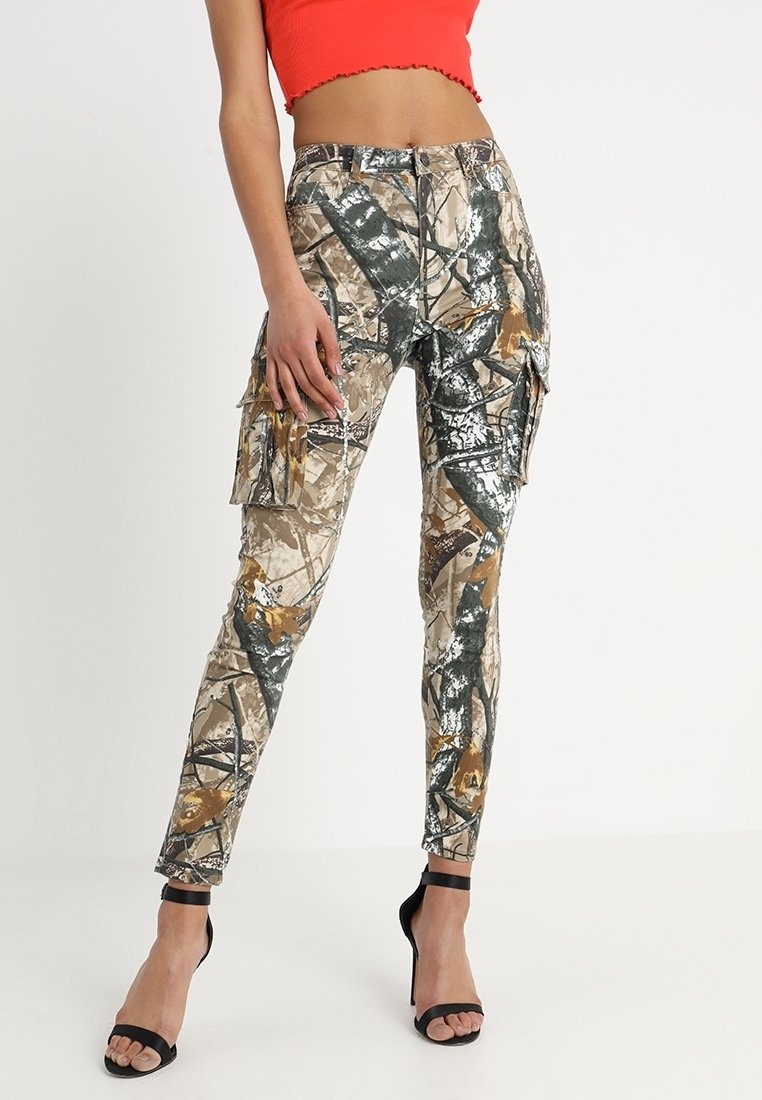 Femme portant un pantalon cargo camouflage beige et vert, un top court rouge et des sandales à talons hauts à bride noire.