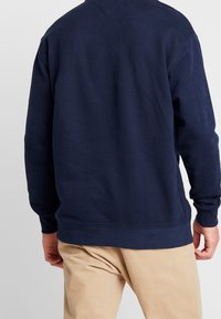 Felpa blu navy con polsini e orlo a costine, caratterizzata da una vestibilità comoda e una texture morbida. I dettagli includono un collo a V e una cucitura sulla schiena.