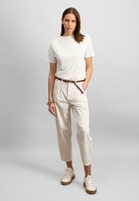 T-shirt bianco a maniche corte abbinato a pantaloni a vita alta di colore crema e sneakers platform bianche. Una cintura marrone arricchisce l'outfit.