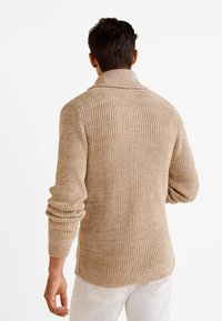 Pull en maille beige texturée avec un col montant, un design côtelé et des manches longues ; doté d'un ourlet droit et de poignets extensibles.