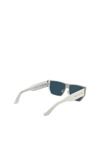 Des lunettes de soleil avec une monture en métal argenté, des verres vert foncé et des branches en plastique blanc. Elles présentent un logo sur le côté et un design géométrique.