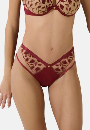 Lingerie en dentelle florale rouge et nude avec des détails transparents, mettant en avant une taille en V et un tissu lisse. Agrémenté d'un petit emblème doré.