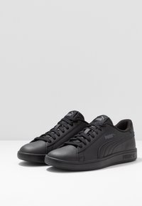 Zapatillas negras con una parte superior de cuero liso, punta redonda, suela de goma plana y cordones. Presentan un logotipo sutil en el lateral y la lengüeta.
