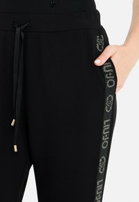 Zwarte joggingsbroek met een geribde tailleband, een trekkoord, zijzak en een decoratieve sprankelende logo-streep langs het been.