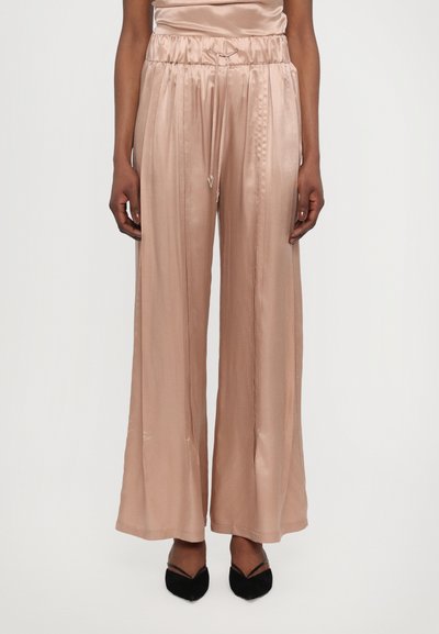 Pantaloni largi din satin în tonuri de roz deschis, cu talie elastică, șnur de ajustare și pliuri verticale; asortați cu balerini negri cu vârf ascuțit.