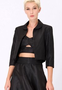 Veste noire courte avec un col arrondi, des manches trois-quarts, une texture lisse et un design minimaliste. À associer avec un haut noir structuré.
