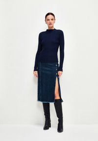 Marinblå ribbad tröja parat med en mörk denimkjol med sidoklyfta och knappdetaljer, kompletterad med knähöga svarta stövlar.