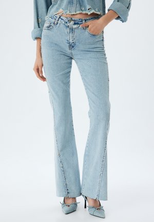 Jeans de campana azul claro con detalles desgastados, dobladillo sin terminar y costuras en contraste. Combinados con tacones de punta afilada azul claro.