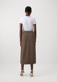 Brown midi skirt made of textured fabric, featuring a high waist, back pockets, and a straight silhouette, paired with a white short-sleeve shirt.