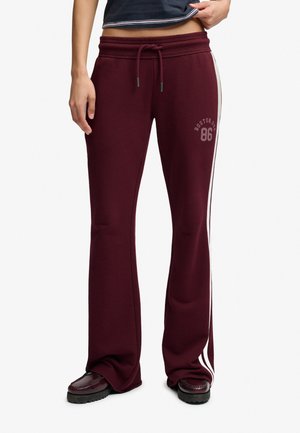 Pantalones deportivos granate con rayas blancas en los laterales, cintura con cordón, texto "Boston 86" en el muslo, combinados con zapatos oscuros y top negro cropped.