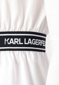 Tessuto bianco con design arricciato, caratterizzato da un'ampia fascia elastica nera con la scritta "KARL LAGERFELD" in bianco e strisce di accentuazione.