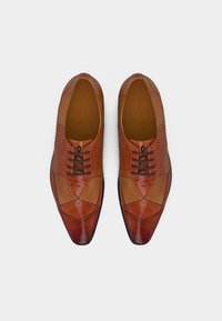 Καφέ δερμάτινα παπούτσια για άντρες με υφή κολάζ και σκουρόκαφέ κορδόνια, απεικονιζόμενα από πάνω σε λευκό φόντο.