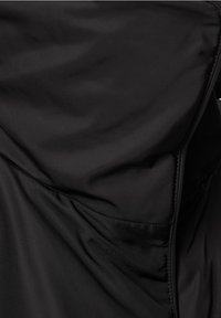 Černá lehká bunda s hladkou texturou, minimalistickým designem, obsahující skryté kapsy a elegantní, bezšvové šití.