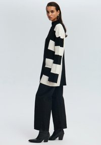 Zwart en crème geribbelde turtleneck trui met blokpatroon, gecombineerd met hoge taille zwarte wijde broek en puntige haklaarzen.