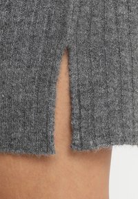 Tessuto grigio a maglia con righe verticali, caratterizzato da una fessura laterale che rivela la pelle sottostante, mostrando una texture morbida e un design casual.