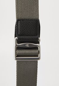 Gray woven fabric belt featuring a black textured leather patch and a silver metal buckle with a logo. Smooth finish and sturdy design.