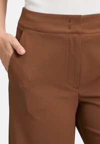 Pantaloni marroni su misura con tasche frontali, dettagli di cucitura sottili, una superficie liscia e una vita aderente.
