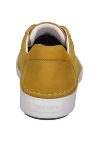 Zapatilla de ante amarilla con parte trasera redondeada, suela blanca y costuras en contraste. El interior cuenta con un forro negro para mayor comodidad.