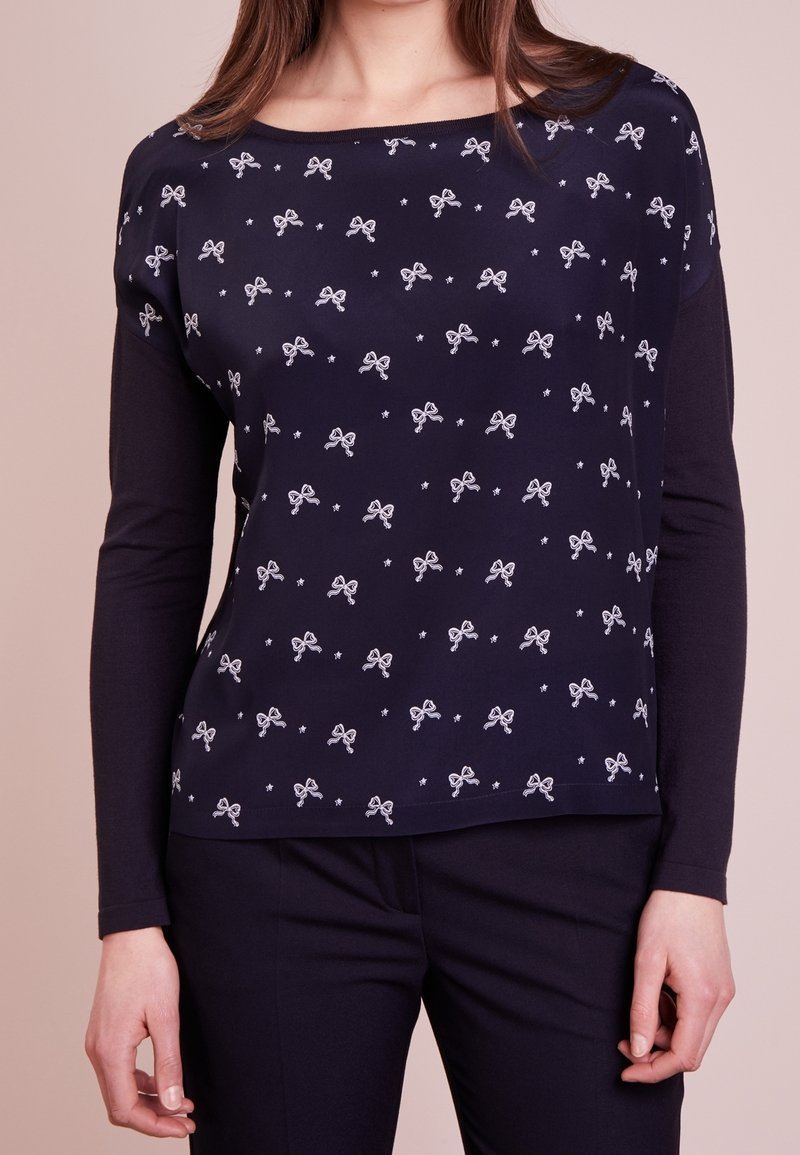 Top a maniche lunghe navy con un design aderente, motivi a fiocco bianchi sparsi e un ampio scollo. Tessuto morbido con una superficie liscia.