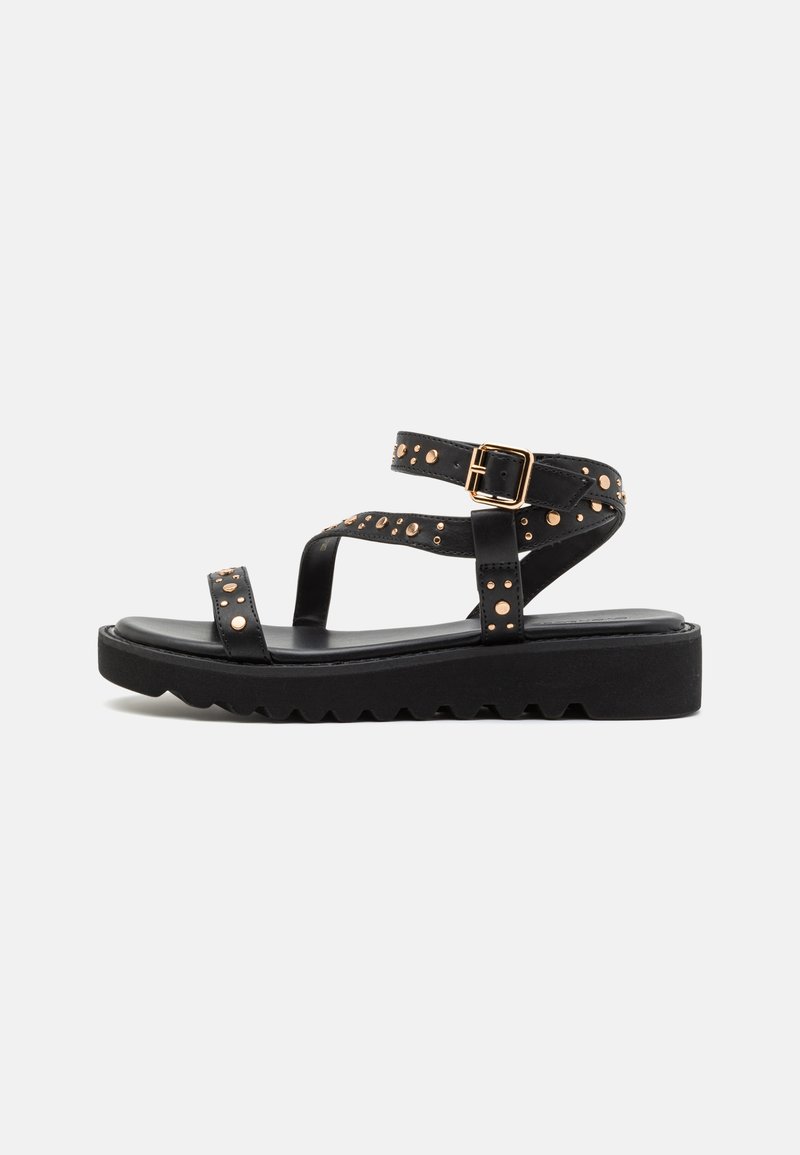 Svarte flate sandaler med flere stropper, med en spenne og gullfargede nagler. Teksturert såle med et rillmønster for bedre grep.