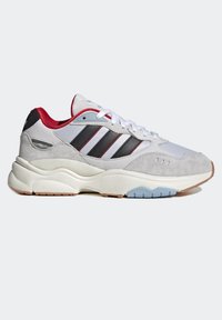 Vit och grå sneaker med röd kant, svarta ränder, vita snören och tjock sål i krämfärg med ljusblå och beige mönstrade detaljer.