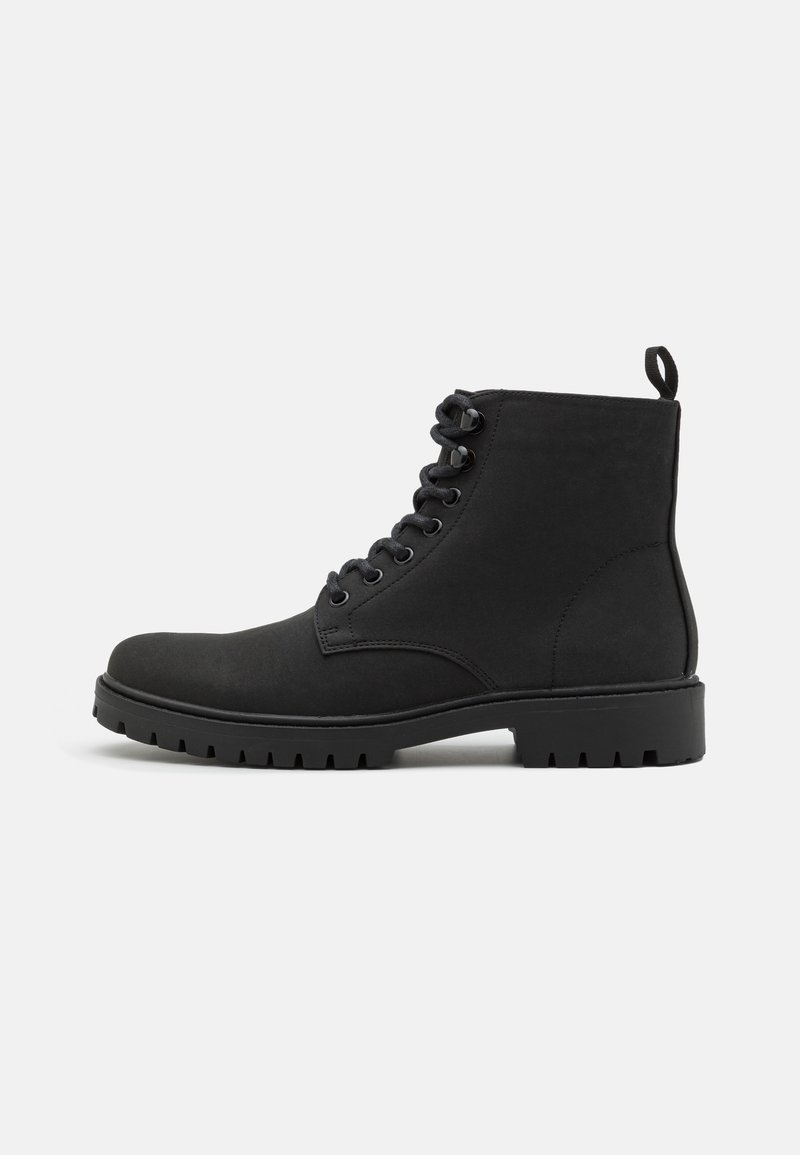 Botas negras de tobillo hechas de material suave, con punta redonda, diseño de cordones y una suela de goma resistente con un patrón de relieve.