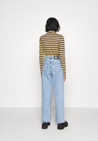 Randig långärmad skjorta med gula och lila ränder; högmidjade ljusblå jeans; svarta klumpiga skor; bakifrån.