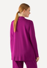Lila Blazer mit langen Ärmeln, entspannter Passform, glatter Textur und Reverskragen, kombiniert mit passenden Hosen. Silberne Creolen werden getragen.