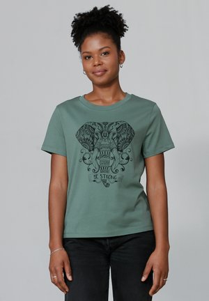 Groene katoenen T-shirt met een zwart olifant graphic en ingewikkelde patronen, met de tekst "WEES STERK" onder het ontwerp. Korte mouwen.