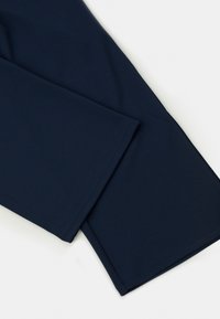 Close-up van donkerblauwe stoffen broeken met nette zomen en een soepele textuur op een witte achtergrond.