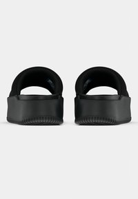 Μαύρα παντόφλες με λείο καουτσούκ εξωτερικό, παχύ μαξιλαρωμένο τακούνι και χαμηλό προφίλ. Στρογγυλεμένη πλάτη χωρίς ορατό μηχανισμό.