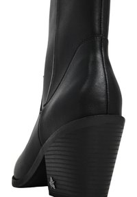 Bota de tacón cuña de cuero negro con suela apilada y pequeña decoración de estrella metálica cerca de la base del tacón.