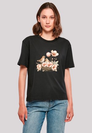 Black cotton t-shirt featuring a graphic of two birds in a nest surrounded by pink flowers. Relaxed fit with short sleeves and round neck.