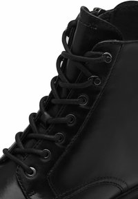 Stivaletti neri in pelle con una texture liscia, occhielli in metallo e lacci neri. Progettati con una punta rotonda e colletto imbottito.