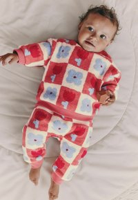 Mukava kaksiosainen asu, jossa on punakeltaiset ruudut ja siniset kukat. Pehmeää fleece-materiaalia, röyhelöillä varustetut hihansuut ja joustava vyötärö.