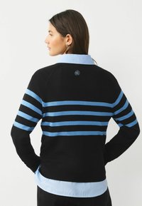 Black sweater with blue stripes, featuring a blue collared shirt underneath. Includes an embroidered logo on the back.